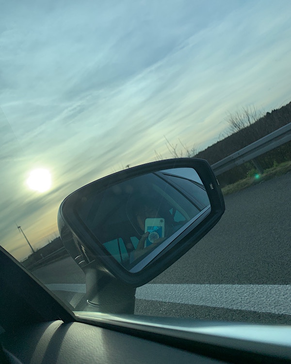 Autorückspiegel mit Sonne am leicht bewölkten Himmel